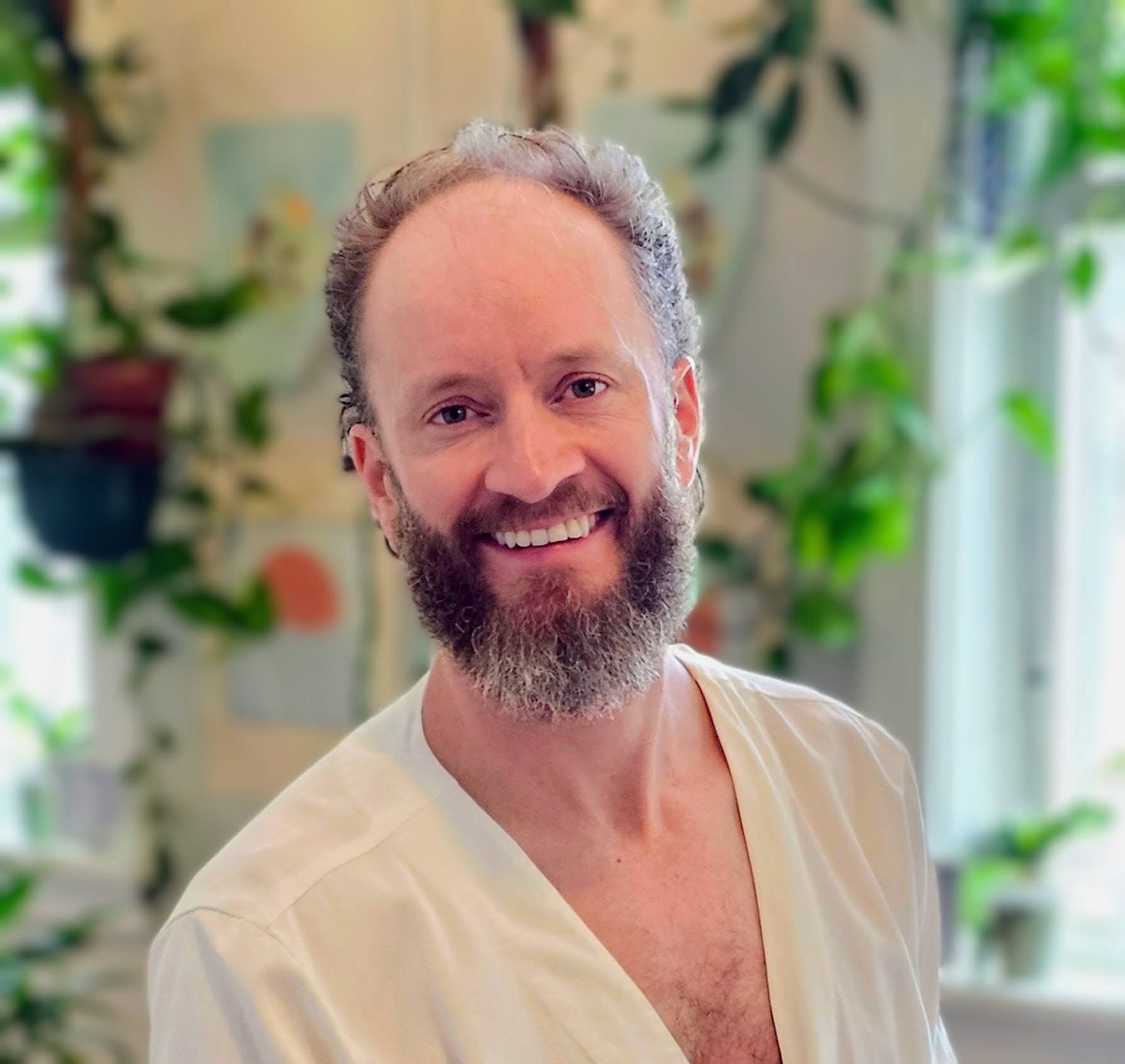Courage smiling in the studio, plants softly out of focus behind him